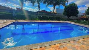 A rectangular swimming pool with a tiled edge, surrounded by a fence and trees.