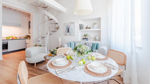 A modern dining area with a round table set for four, surrounded by wicker chairs. A spiral staircase is visible in the background, leading to an upper level. - Luxury 2 Bedrooms 2 Bathrooms Penthouse, Elevator (Lucca)