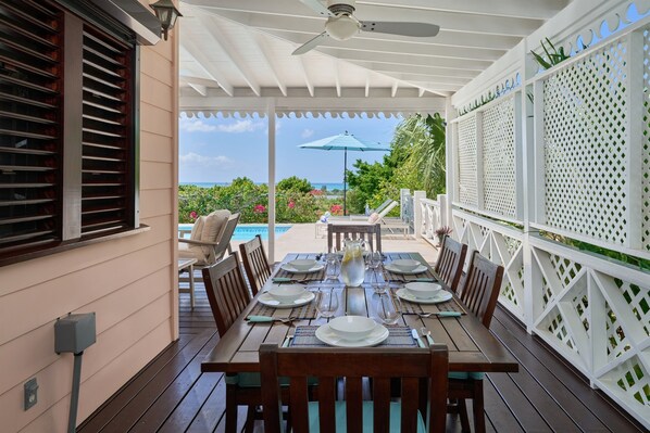 Un espace extérieur abrité, aménagé pour les repas, avec une table pour six personnes, donnant sur une piscine et un jardin.