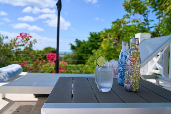 A table with a water bottle, a glass with a lime slice, and two insulated bottles with tropical designs.
