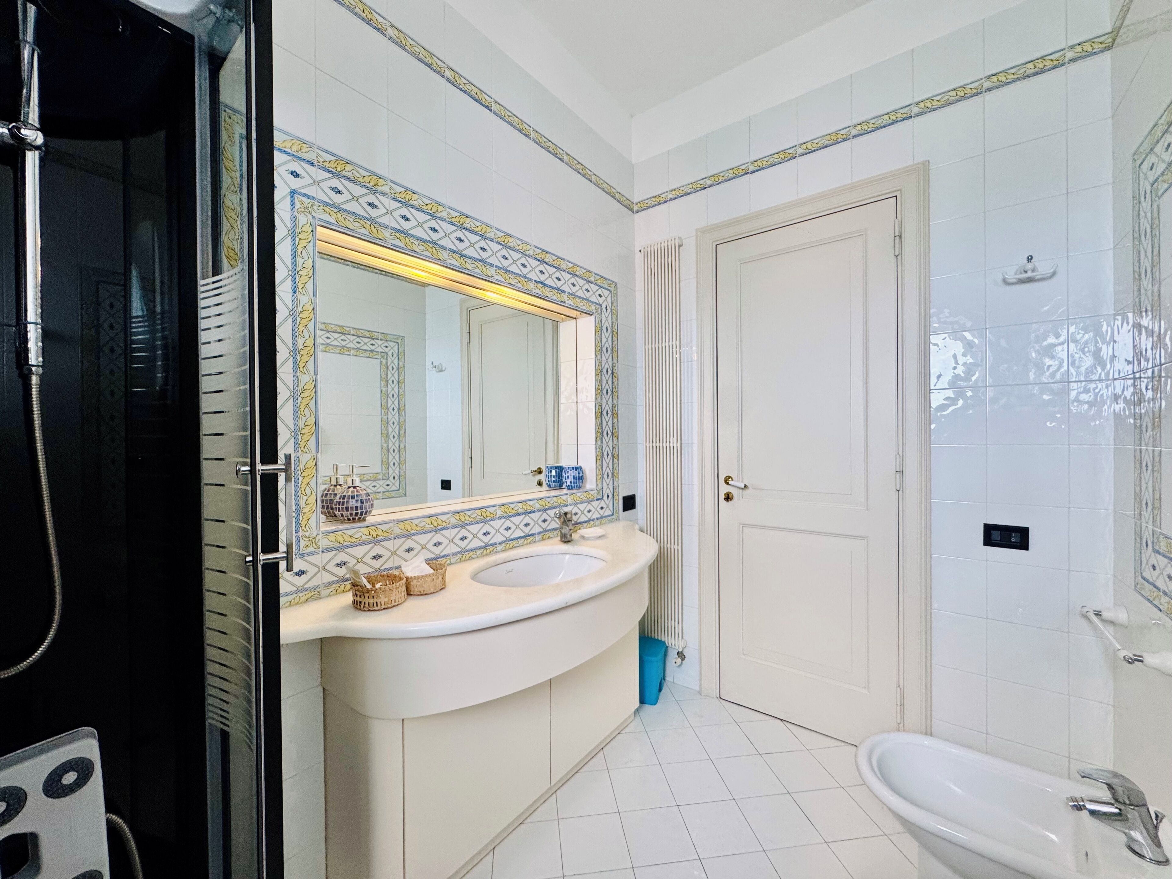 A bathroom with a white sink, a mirror with decorative tiles, a shower, and a toilet.