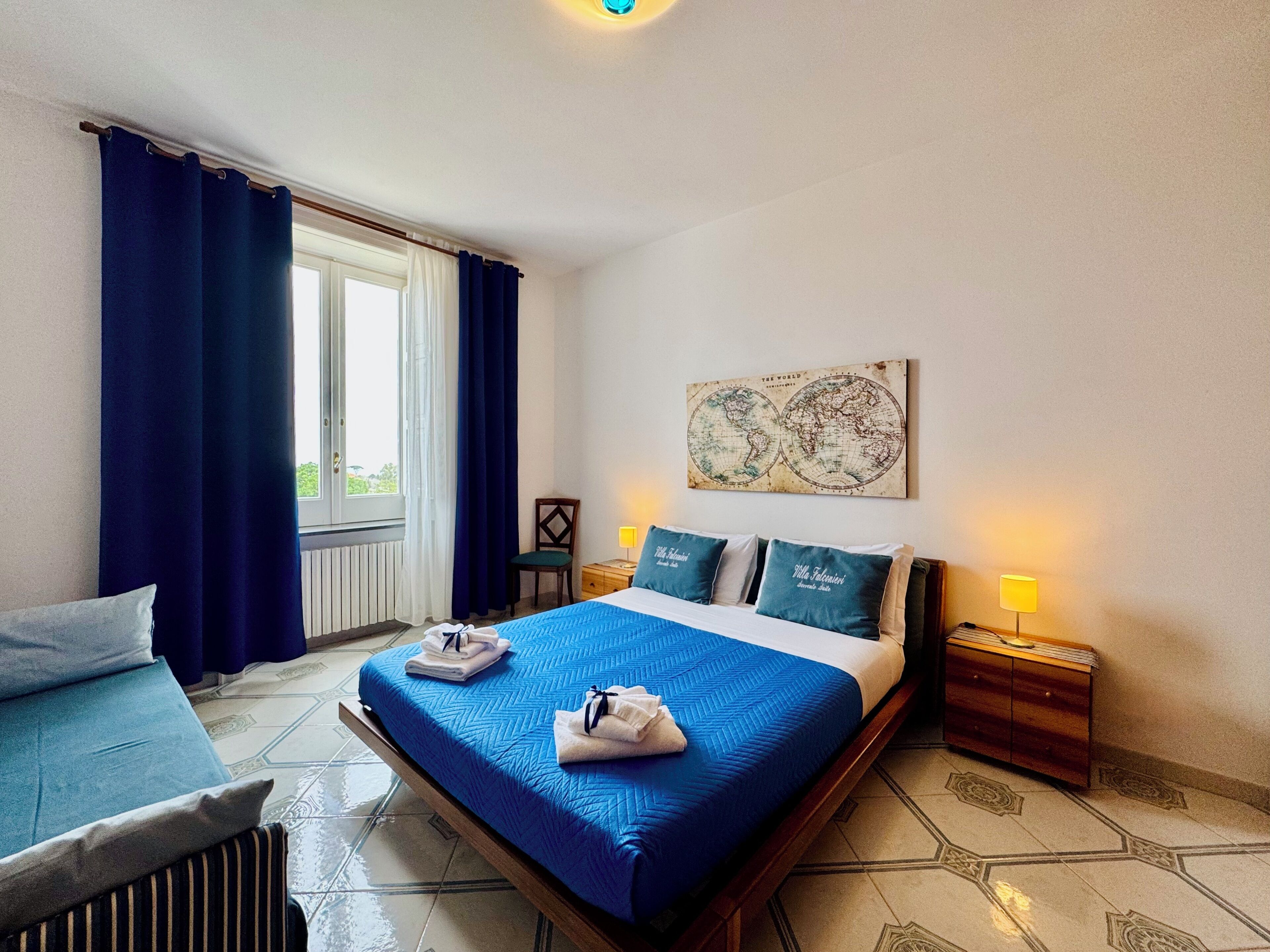 Una habitación de hotel con una cama, una silla, un mapa en la pared y una ventana con cortinas.