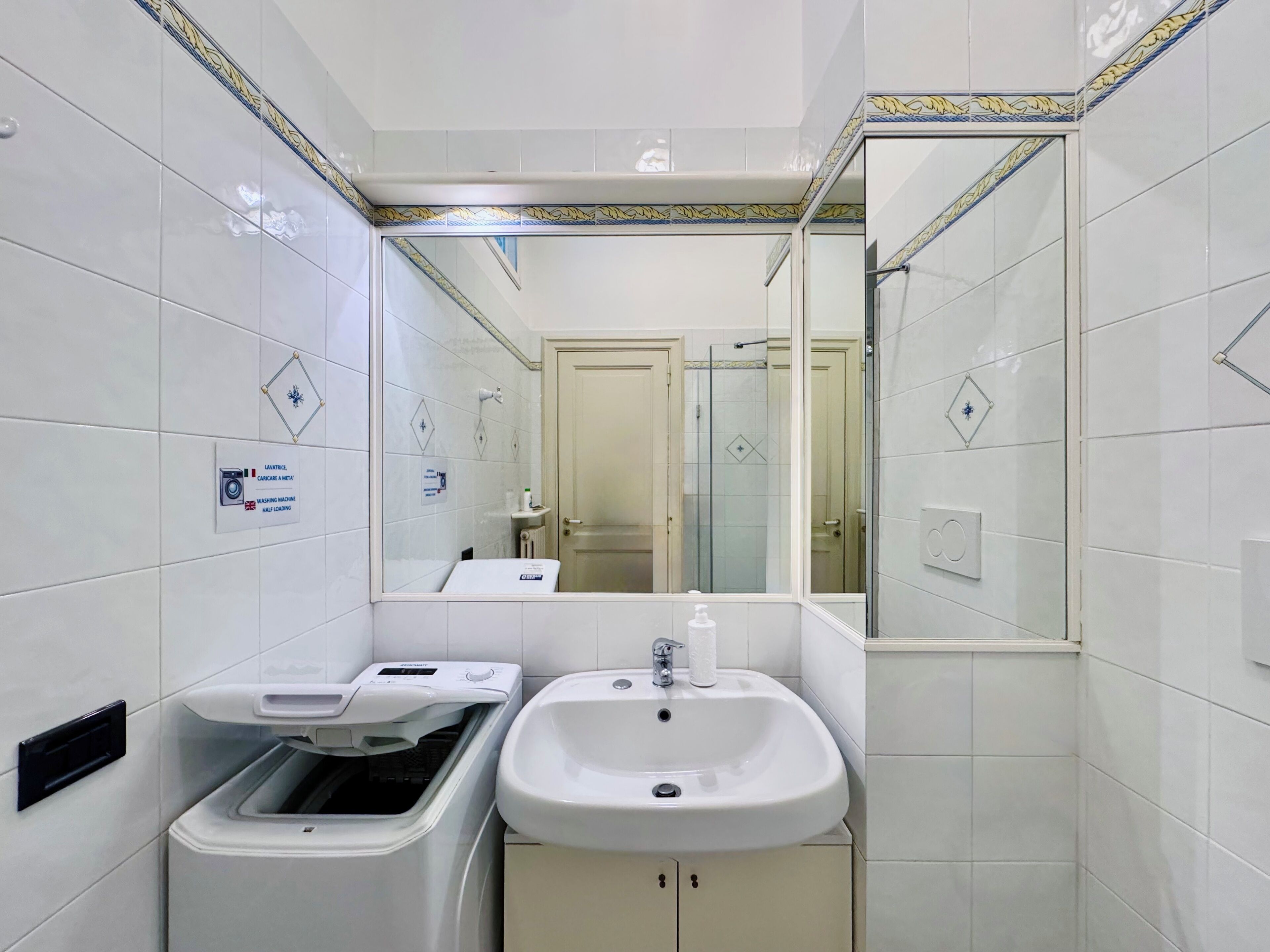 Un baño pequeño con lavadora, lavamanos y espejo.
