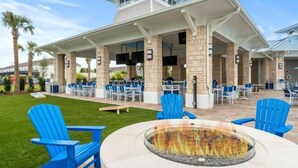 An outdoor patio area with blue Adirondack chairs, a fire pit, and a covered seating area with tables and chairs.