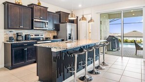 A modern kitchen with dark cabinetry, a large island with bar stools, stainless appliances, and a view of a swimming pool.
