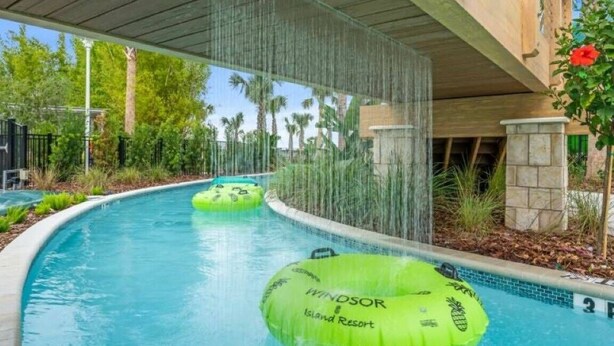 A pool area with a wooden canopy, green inflatable rings, and a stone wall.