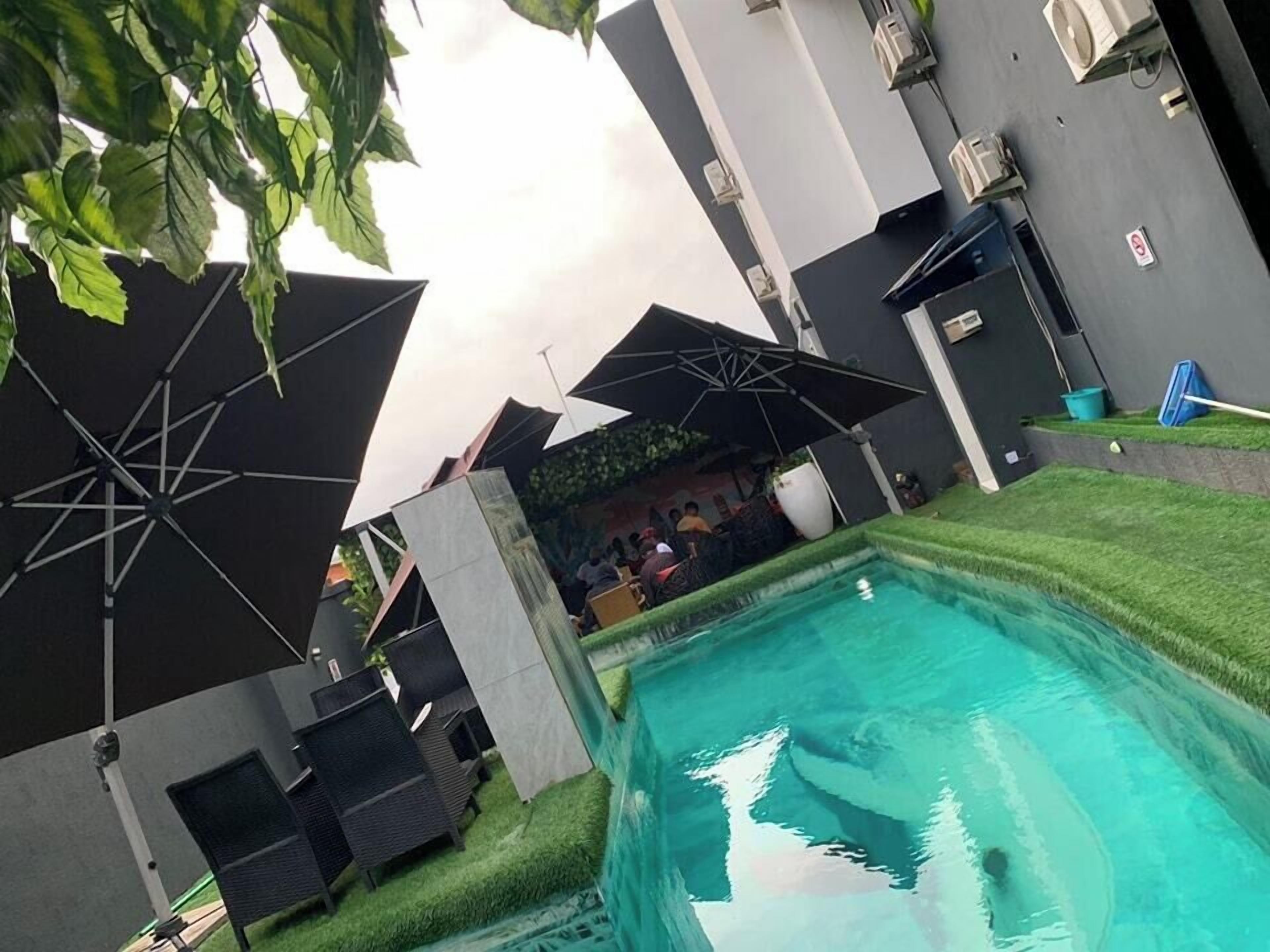 A pool area with multiple umbrellas, lounge chairs, and a clear blue pool.