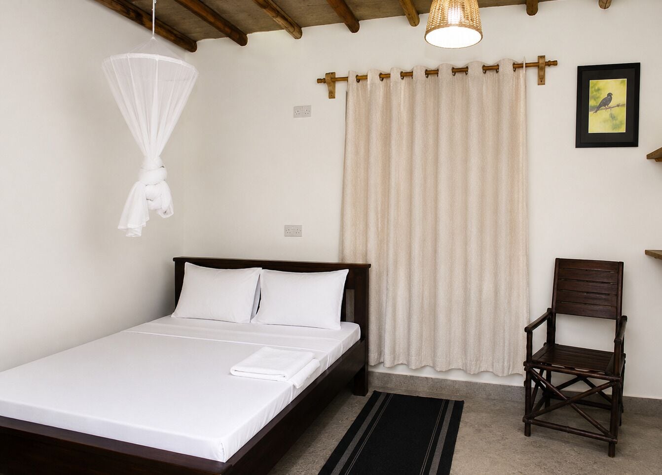 A bedroom with a bed, a chair, a hanging mosquito net, and a curtain.