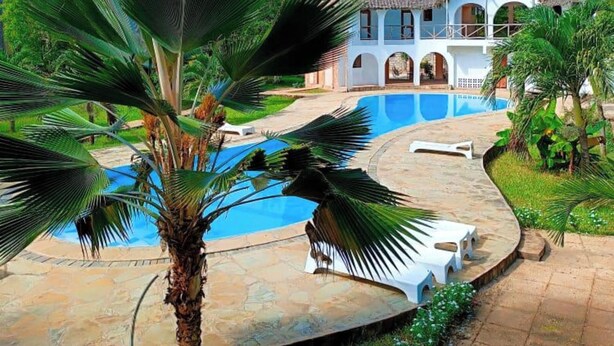 A resort with a pool, palm trees, and a large house with a thatched roof. - Raquel's Bliss Hotel Diani (Diani Beach)