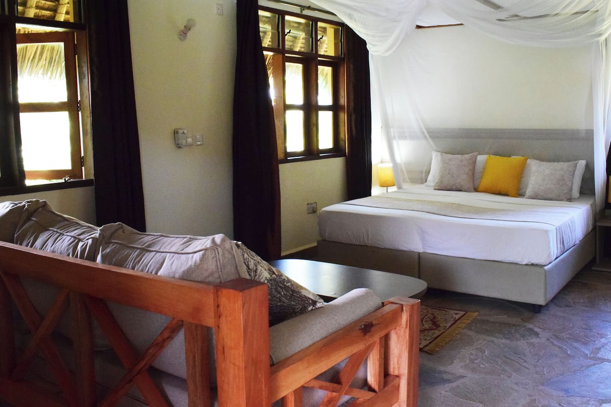 A bedroom with a bed, a wooden bench, and a window with curtains.