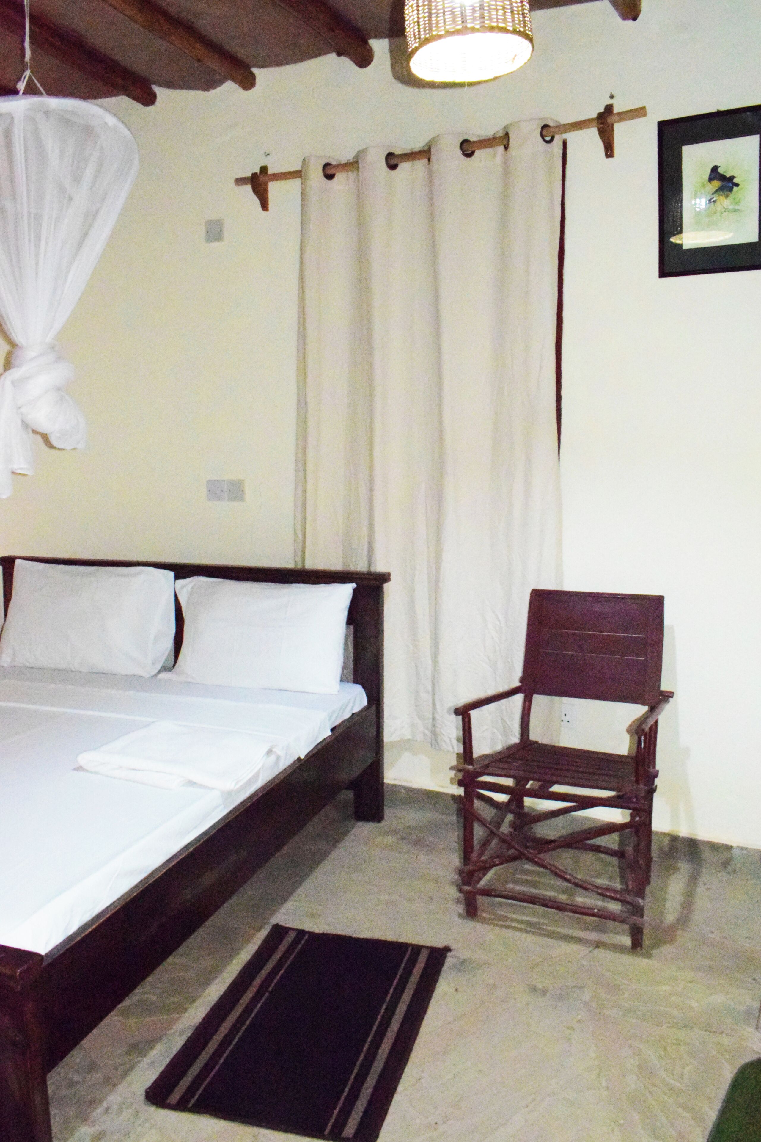 A bedroom with a bed, a chair, a hanging mosquito net, and a picture on the wall.