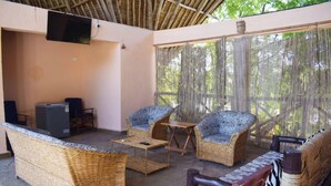 A covered outdoor seating area with wicker furniture, a flat-screen TV, and a table. - Raquel's Bliss Hotel Diani (Diani Beach)