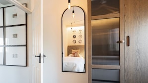 A hotel room with a large mirror, a bed with a headboard, and a wooden door.