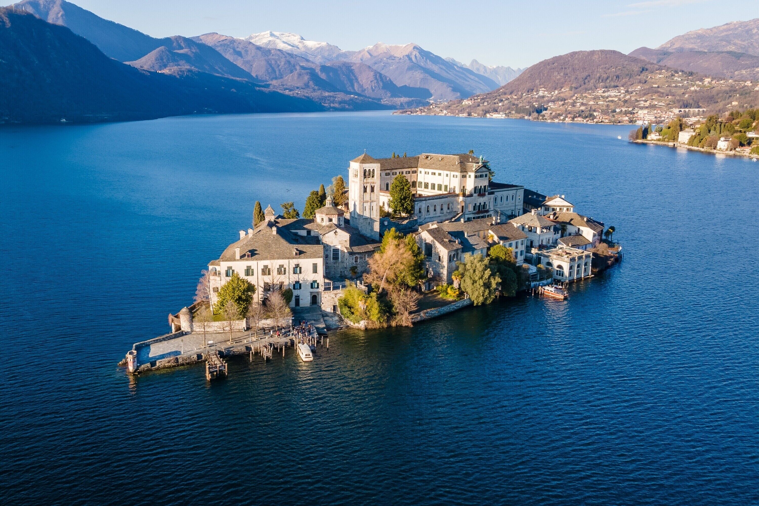 An island hotel with multiple buildings, a dock, and a lake with mountains in the background.