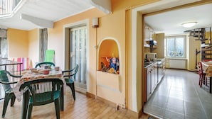 A dining area with a table set for two, chairs, and a window with curtains. - Old Pella: 100m to Lake Orta, Terrace and Views (Pella)