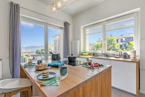A modern kitchen with a large island, a view of the city, and a dining area with a chair.