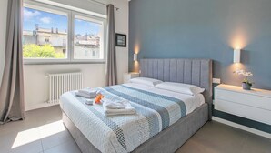 Ein Schlafzimmer mit Bett, Fenster, Heizkörper und einem Nachttisch mit Lampe.
