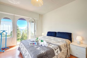 A bedroom with a bed, a nightstand, a lamp, a window with a view, and a towel rack. - Lorenza Rooftop Lake View Stresa (Stresa)