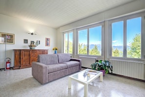 A living room with a sofa, a coffee table, large windows with a view, a wooden cabinet, and a fire extinguisher. - Lorenza Rooftop Lake View Stresa (Stresa)