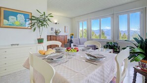 Zona pranzo con tavolo apparecchiato per quattro, un quadro appeso e vista sulle montagne attraverso ampie finestre.
