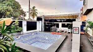 Une piscine extérieure avec un sol carrelé, entourée d’une terrasse en béton et agrémentée de plantes en pot.