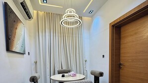 Un coin repas comprenant une table ronde, quatre chaises rembourrées, un luminaire suspendu et une porte en bois.