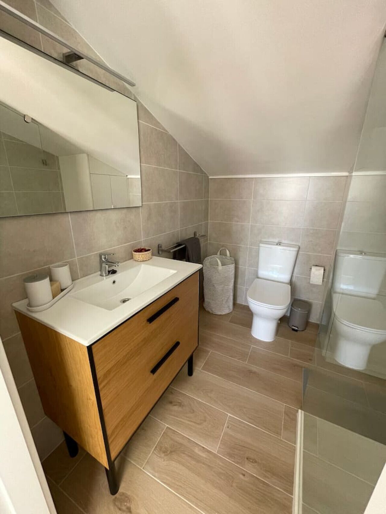 Une salle de bain moderne avec un meuble-lavabo en bois, un grand miroir, des toilettes et un bidet.