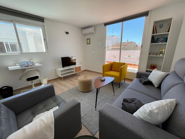 A modern living room with a grey sofa, a yellow armchair, a small round table, and a TV on a stand.