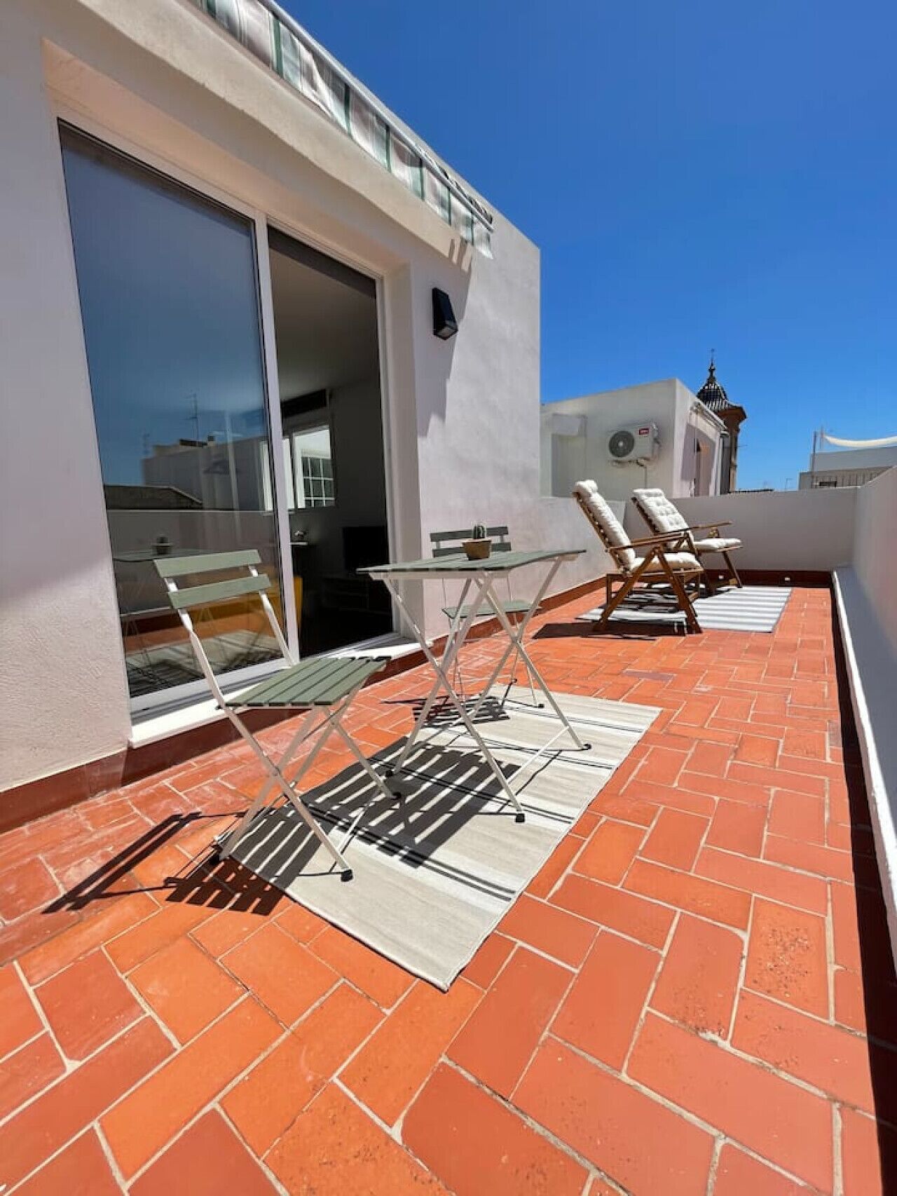 Una terraza en la azotea con piso de ladrillo, una puerta de vidrio que da a un espacio interior y dos sillones de descanso.