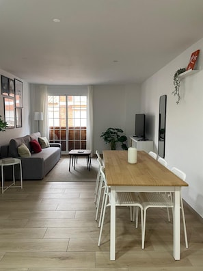 A modern living room with a sofa, dining table, chairs, and a TV.