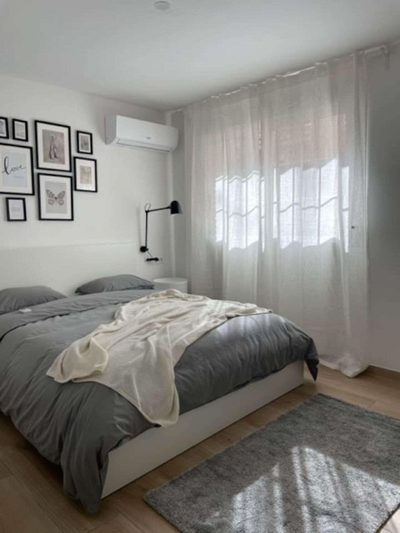 A bedroom with a bed, a bedside table, a lamp, a window with curtains, and framed pictures on the wall.