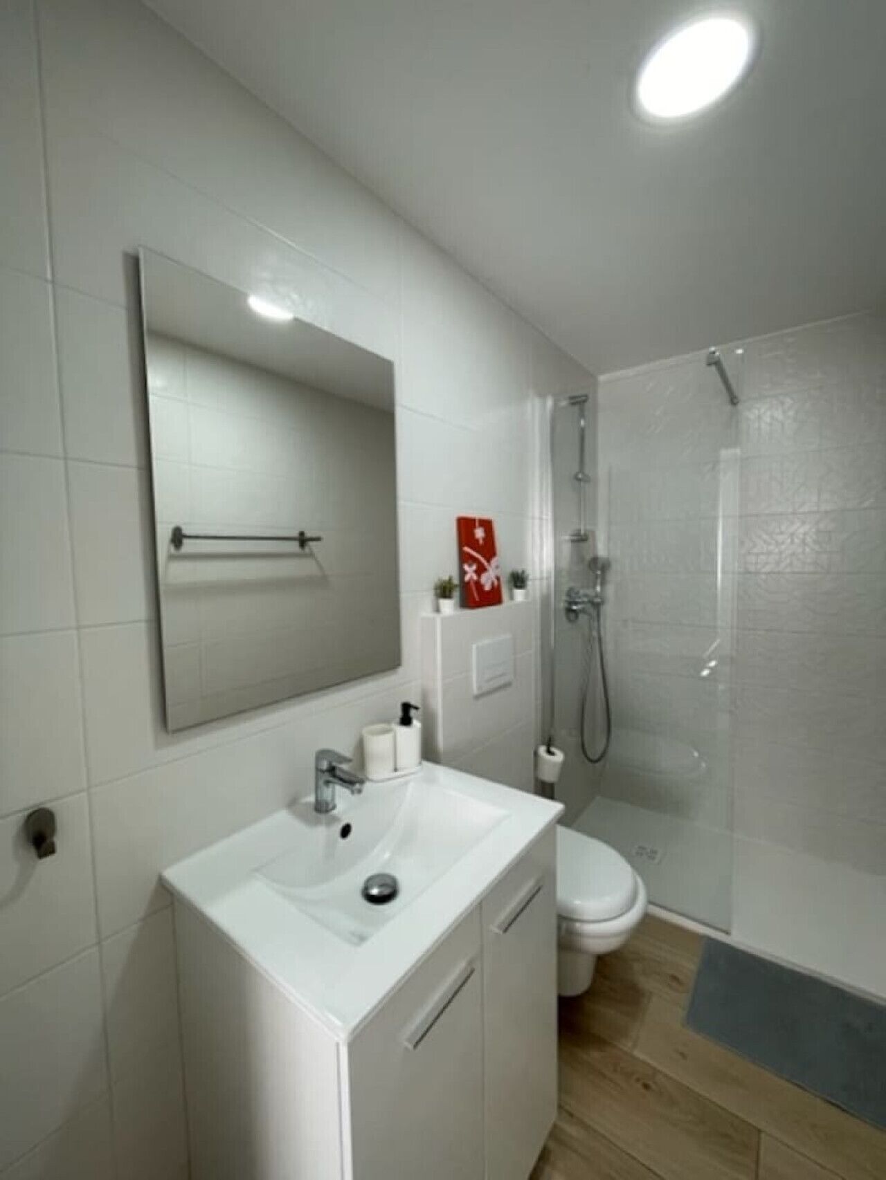 Un baño moderno con un lavamanos, espejo y retrete blancos.