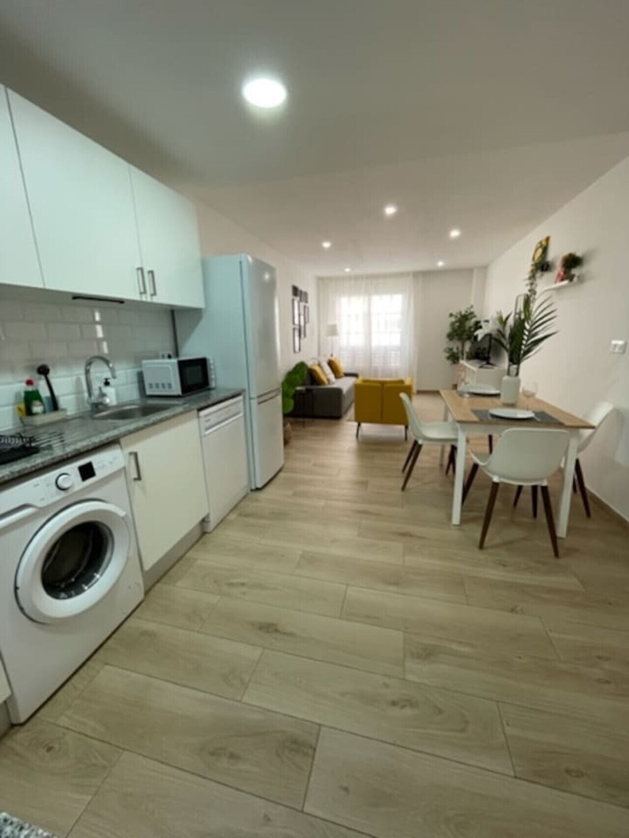 Una cocina moderna con lavadora, un comedor con mesa y sillas, y una sala de estar con sofá.