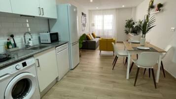 Una cocina moderna con lavadora, un comedor con mesa y sillas, y una sala de estar con sofá.