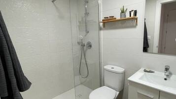 Un baño moderno con ducha de vidrio, inodoro blanco y lavamanos con espejo.