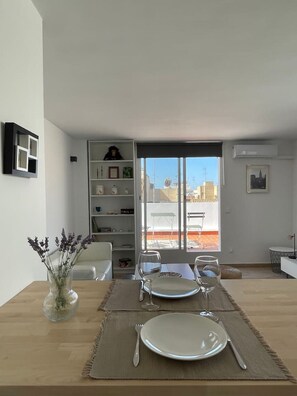 Un comedor con una mesa dispuesta para dos personas, una estantería y vistas de la ciudad a través de un ventanal grande.