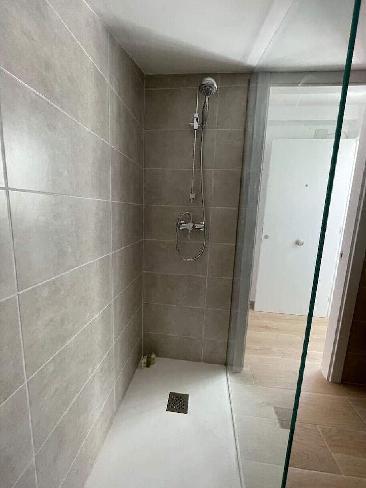 Un petit espace douche fermé, avec des murs et un sol carrelés, une pomme de douche et un panneau de commande.