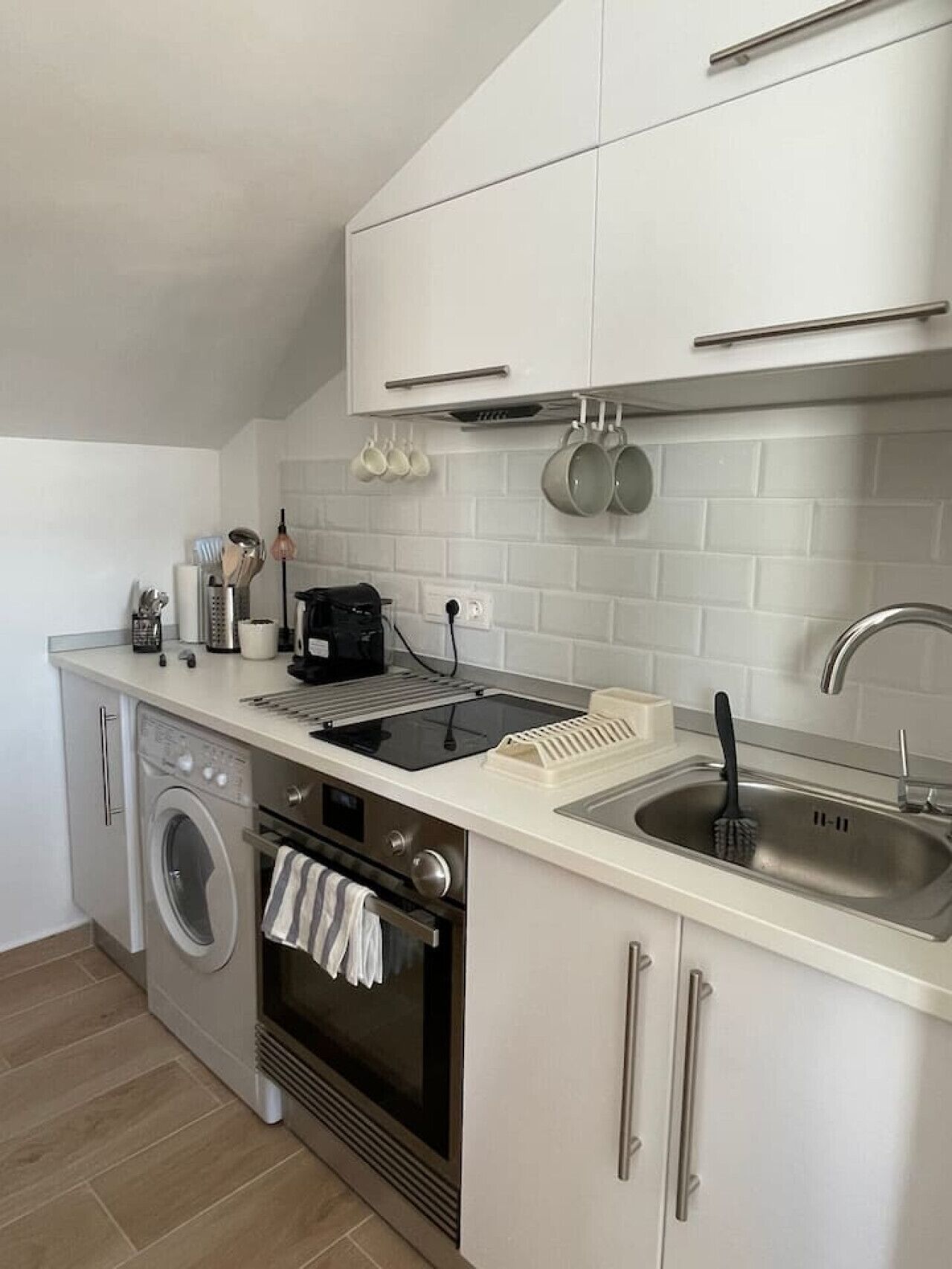 A compact kitchen with a washing machine, oven, and a sink with a dish rack.