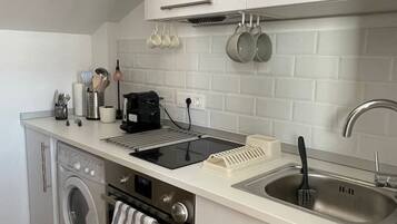 A compact kitchen with a washing machine, oven, and a sink with a dish rack.