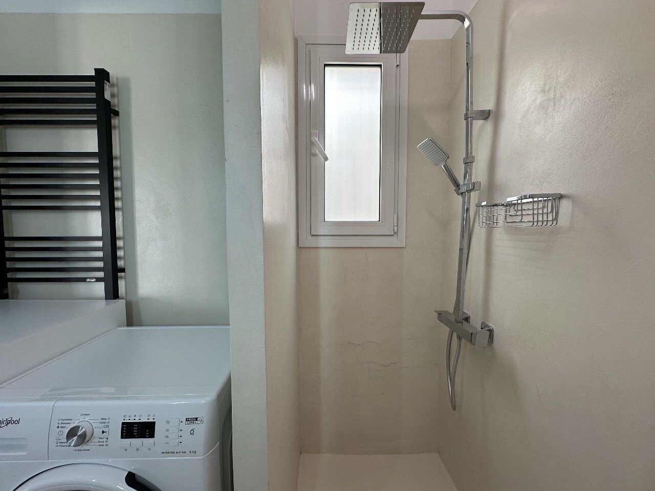 Un espace buanderie comprenant un lave-linge, un étendoir et une douche avec une fenêtre située au-dessus.
