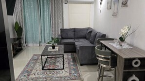 A modern living room with a grey sofa, a coffee table, a dining table with chairs, and a TV mounted on the wall. - Comfy Fresh and Clean Spacious 1- bedroom apartment with AC in charming Portmore (Portmore)