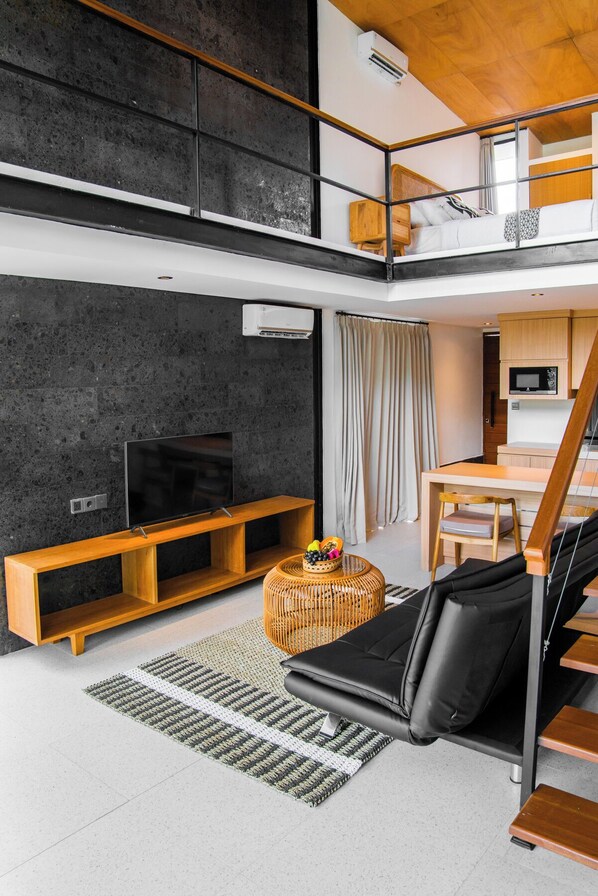Un appartement moderne de style « loft », doté d’un plafond haut, d’un téléviseur à écran plat, d’un coin repas et d’un escalier menant à un niveau supérieur.