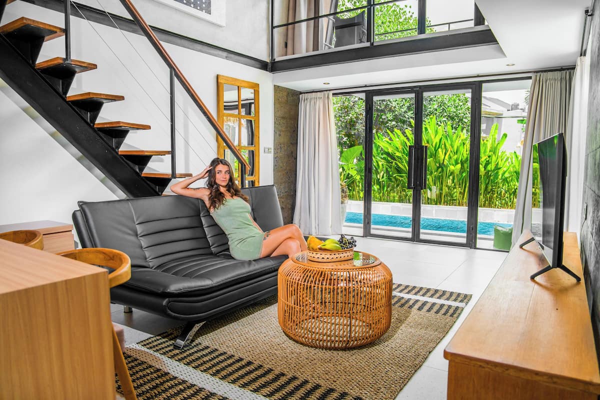 A modern living room with a black leather sofa, a wicker coffee table, and a staircase with wooden steps.