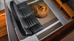 Ein modernes Wohnzimmer mit einem schwarzen Ledersofa, einem Couchtisch mit Früchten und einem Fernseher auf einem Holzständer.
