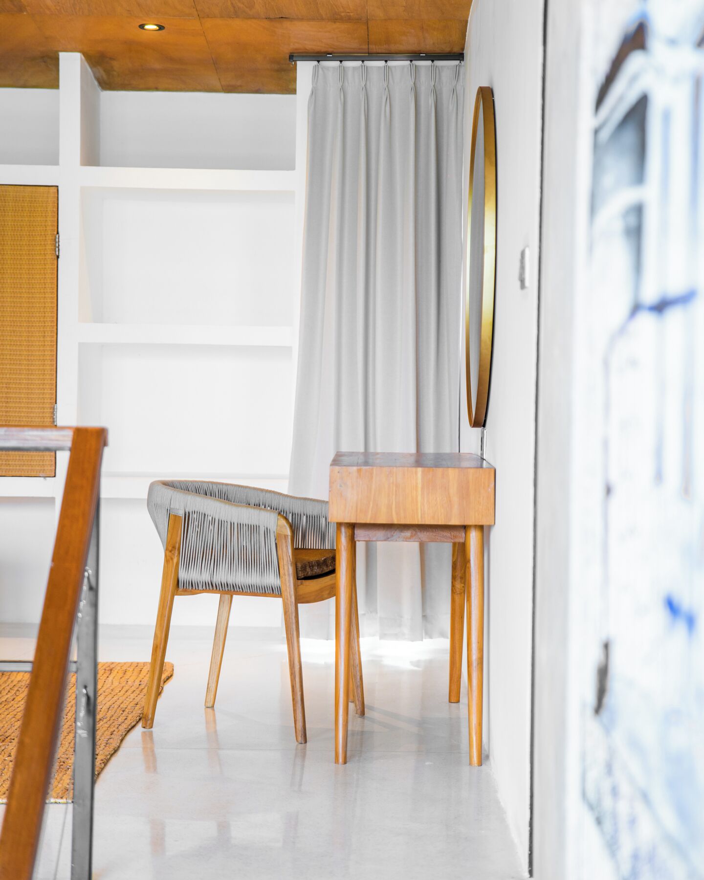 A modern room with a wooden ceiling, a white wall, a grey curtain, a wooden chair, a small wooden table, and a mirror.