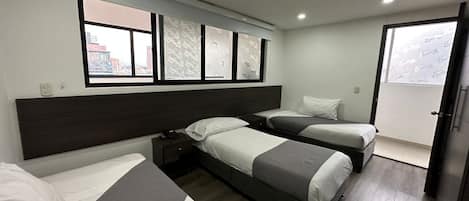 Une chambre d’hôtel avec deux lits simples, une grande fenêtre avec des rideaux à motifs, une tête de lit sombre et une petite table de chevet avec un téléphone.