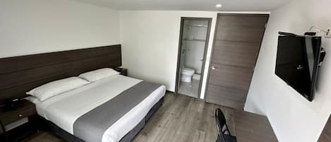 Habitación de hotel con cama, mesita de noche, silla, televisor y puerta que da a un baño.