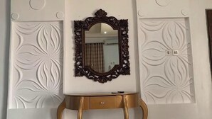 A room with a decorative mirror on a gold stand, flanked by two white walls with embossed floral patterns. - Emsworth Hotels and Apartments  (Abuja)