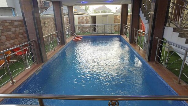 A swimming pool with a blue surface, surrounded by metal railings and a brick wall. - Emsworth Hotels and Apartments  (Abuja)