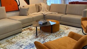 A modern living room with a sectional sofa, a round coffee table, and a large abstract painting on the wall. - Emsworth Hotels and Apartments  (Abuja)
